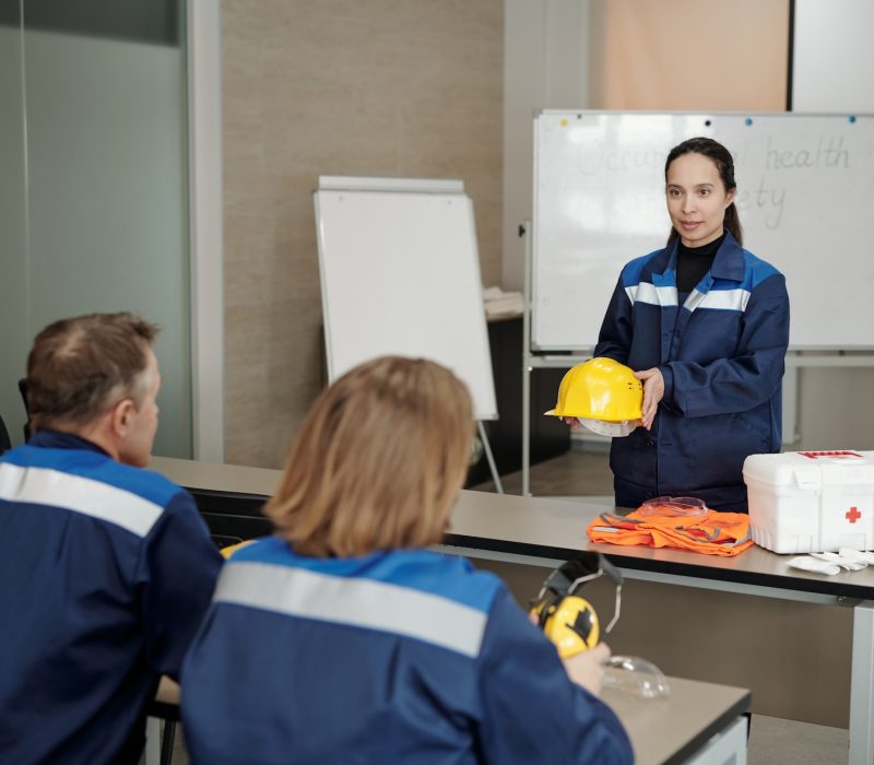 Attractive mixed race woman holding yellow hardhat and telling about personal safety in industry to employees
